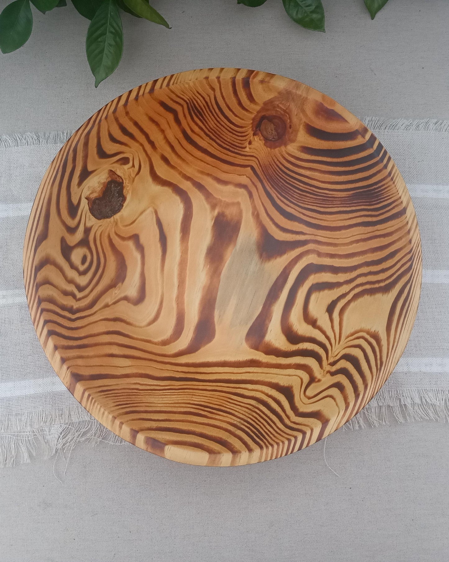 a shallow pine wood bowl that has been charred to blacken the growth rings in the wood while the sapwood remains a pale cream color. resin pockets in the sidewall standout with stunning detail set on a natural linen table runner