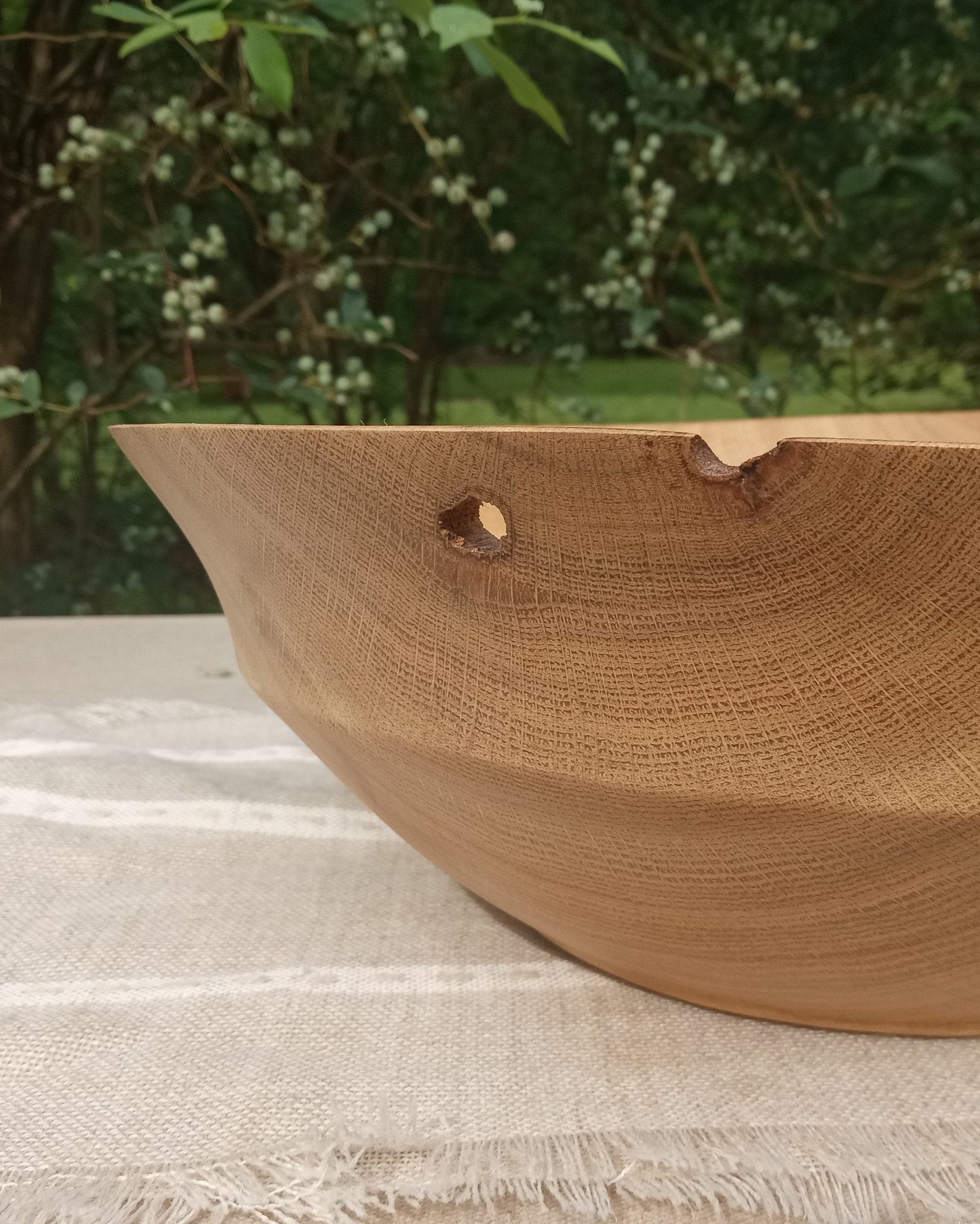 close up of a decoratively carved oak wood bowl with unusual naturally occurring holes in the sidewall and rim about a quarter inch across