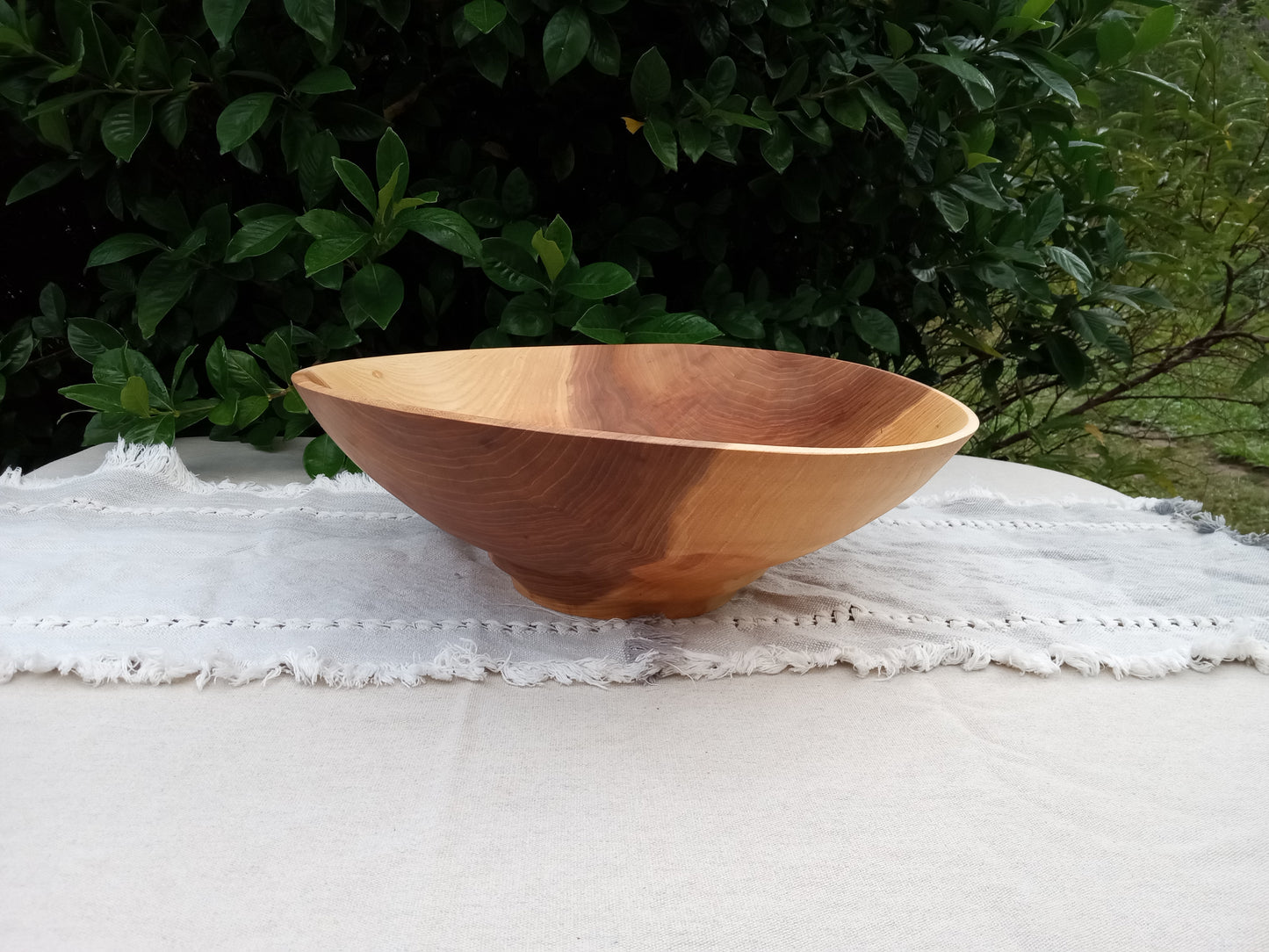 a large natural edge wood bowl with a narrow pedestal base and wide curvy top, highly figured grain pattern and contrasting dark amber tones with creamy sapwood