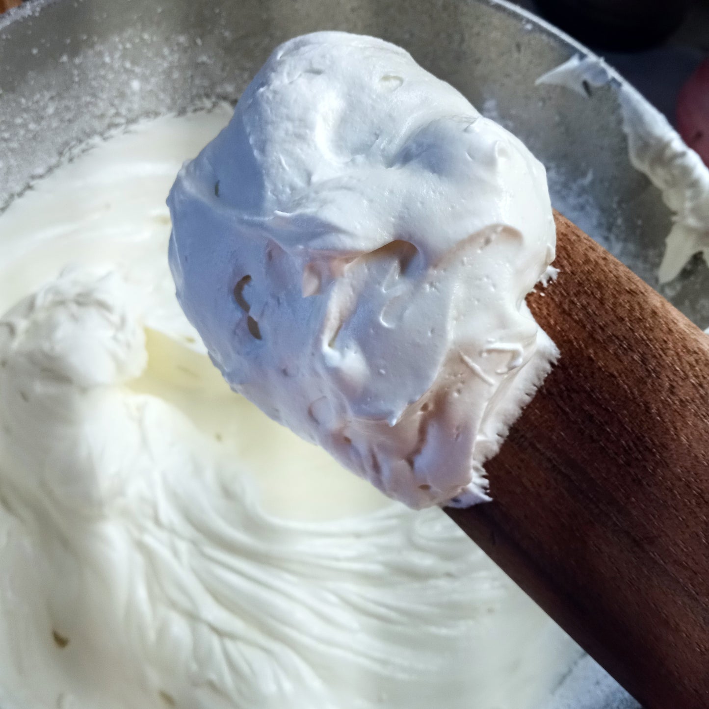 fluffy whipped white body butter on a wooden spurtle taken from a bowl of creamy white body butter below