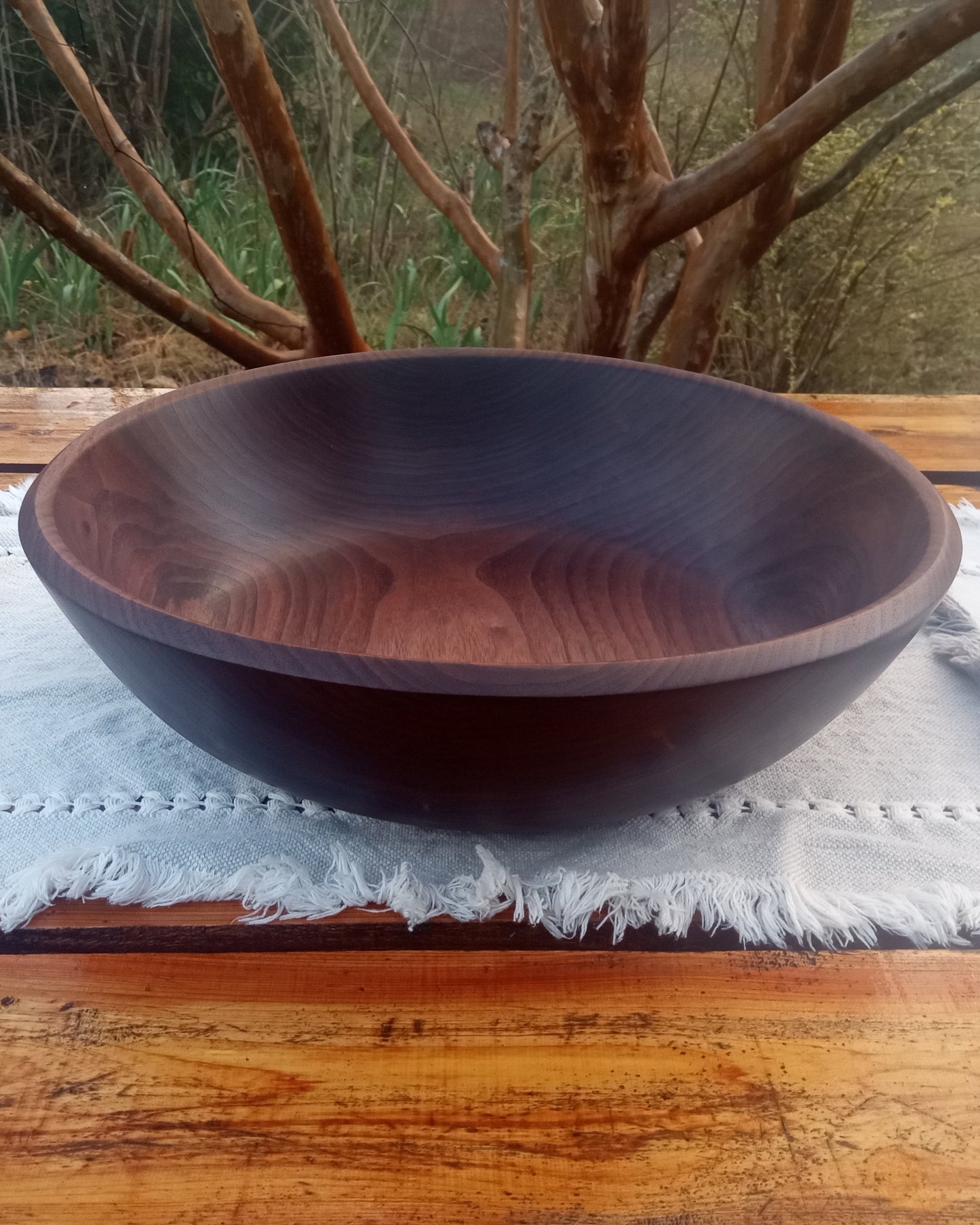 shallow black walnut wood bowl with a finely carved rim set on a rustic wooden table