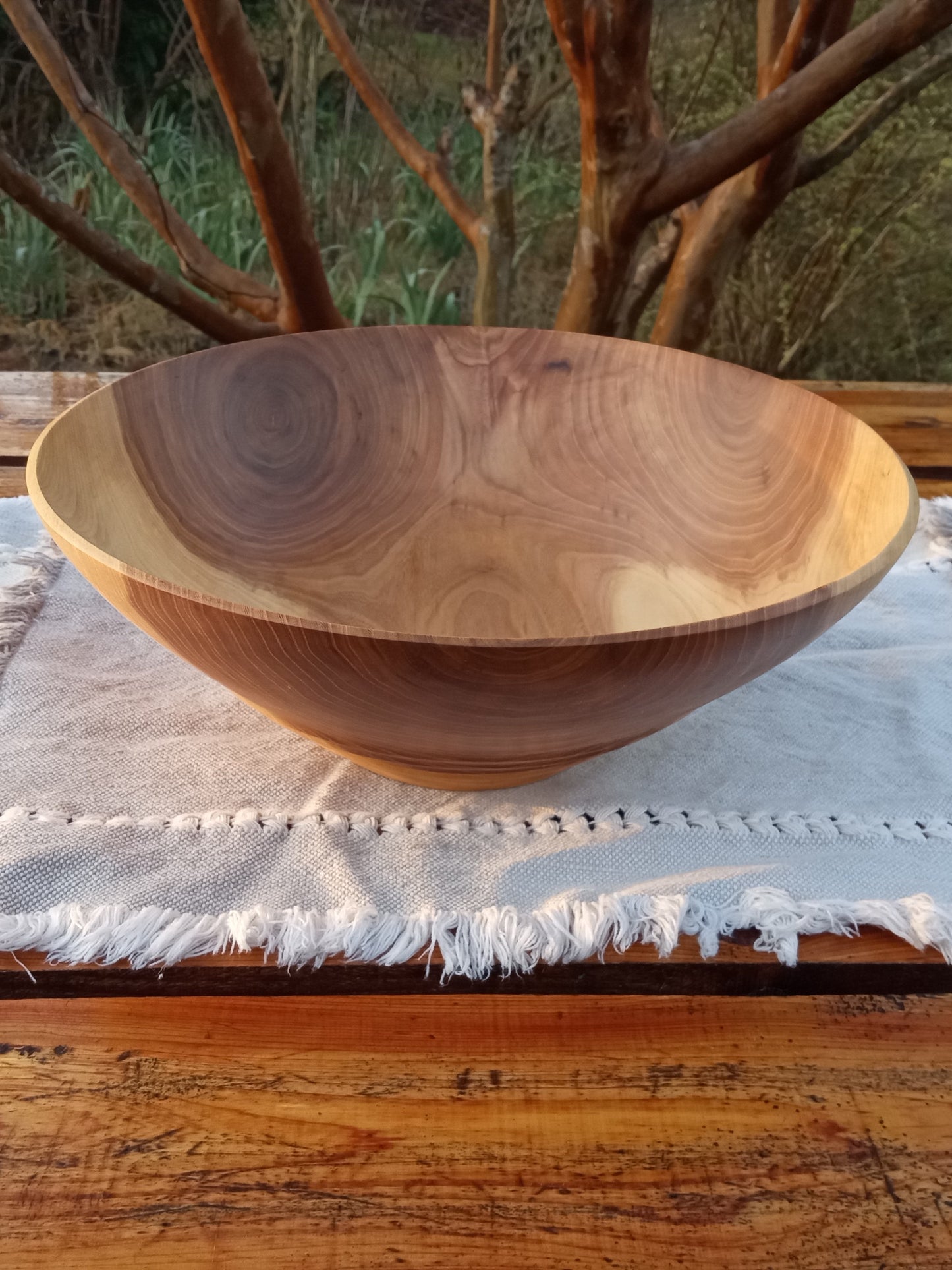 highly figured tapered wood bowl with warm amber heartwood contrasting pale cream sapwood in the sidewall and multiple decorative ridges carved into the bottom set on a rustic wooden table with a pale blue woven runner