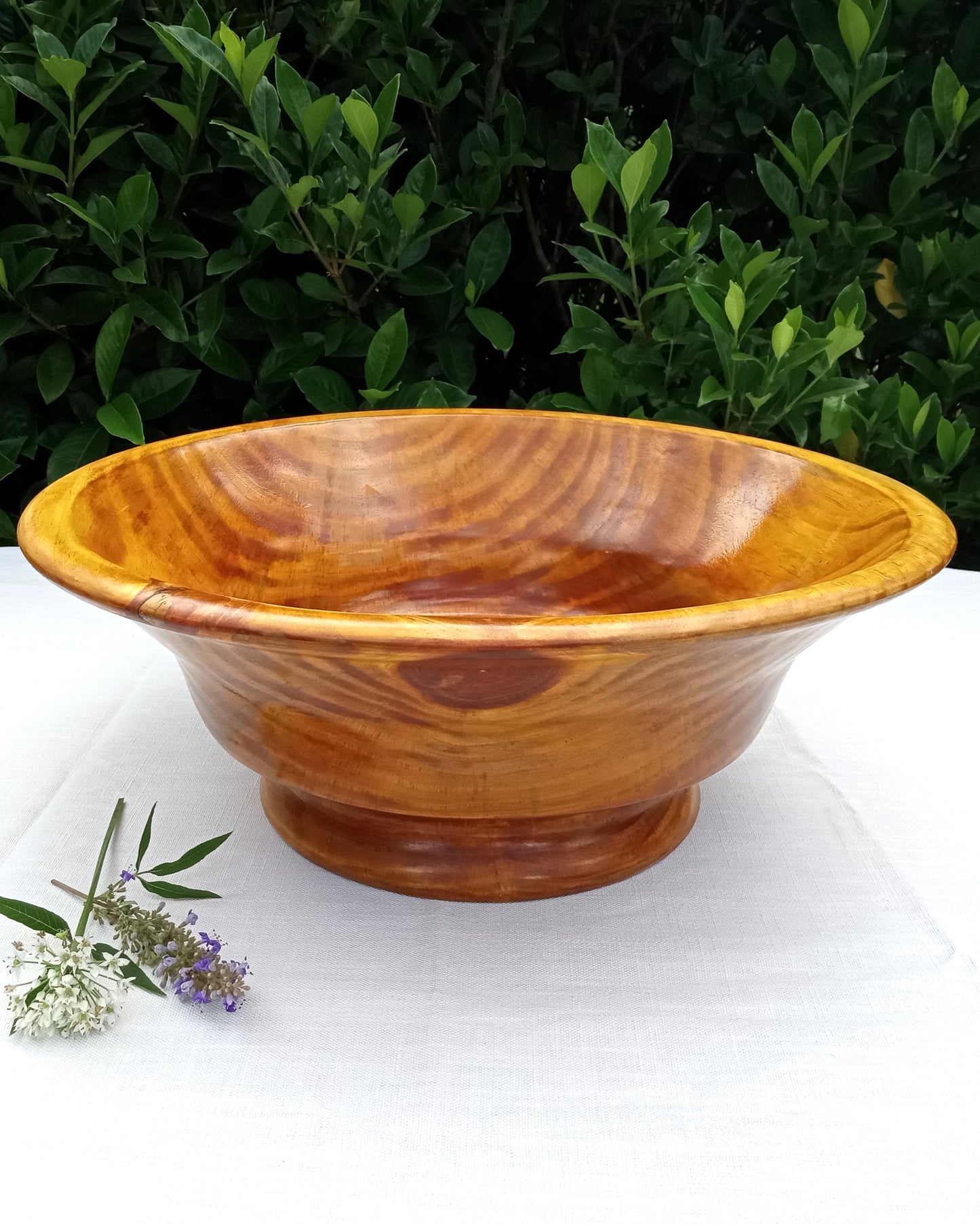 elegant vase shaped wood pedestal bowl dyed a golden yellow hue set on a white tablecloth with flowers beside it