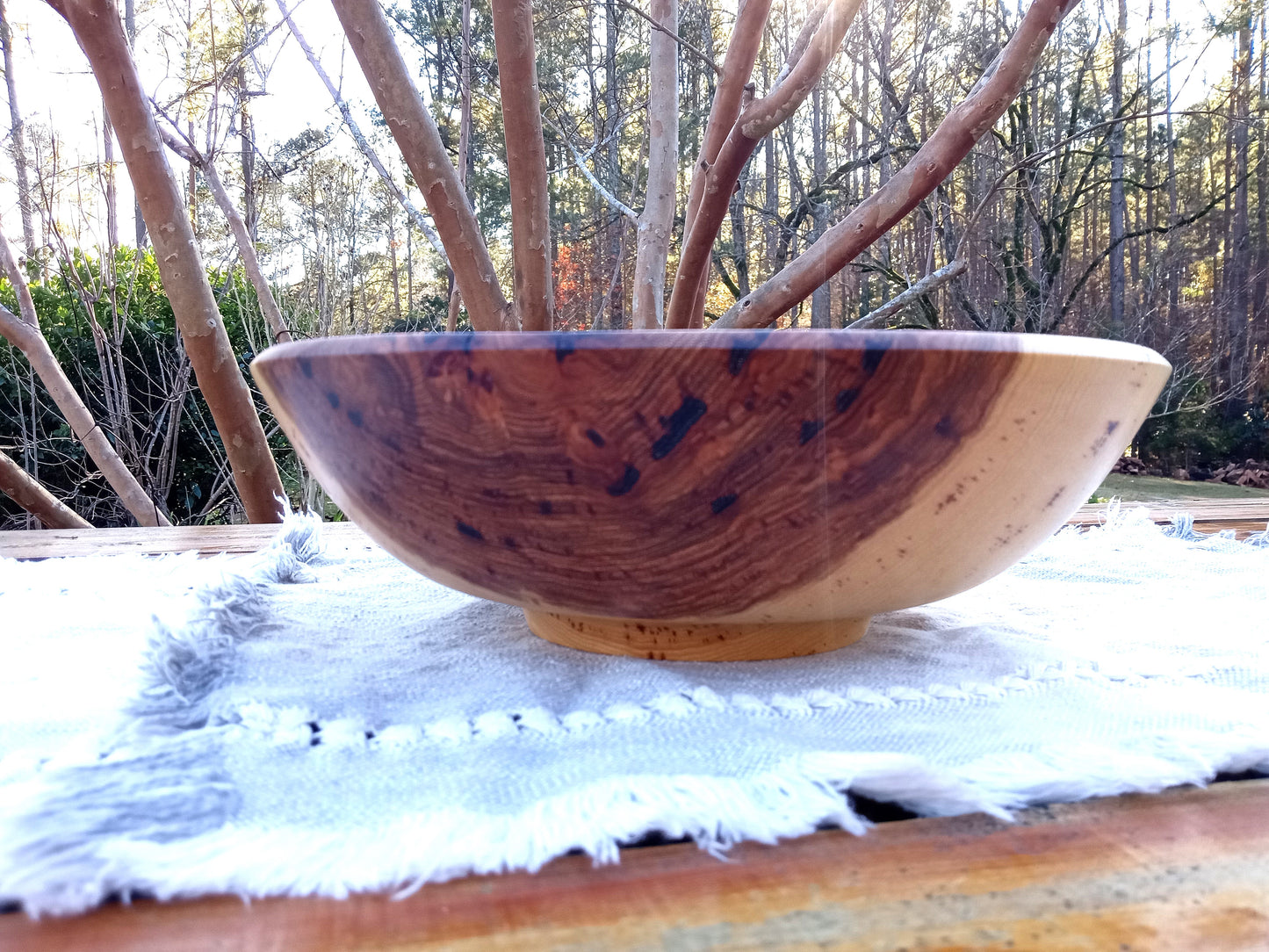 a highly figured hickory burl bowl with deep amber heartwood and cream sapwood contrasts in the sidewall, shaped in an elegant round body design with a pedestal footing set on a woven blue cotton table runner