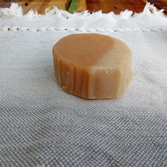a round orange and cream colored bar of soap with wrinkly edges set on a pale blue cotton cloth 
