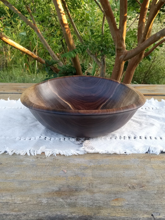 Black walnut bowl on a white cloth against crape myrtle branches with a garden in the background